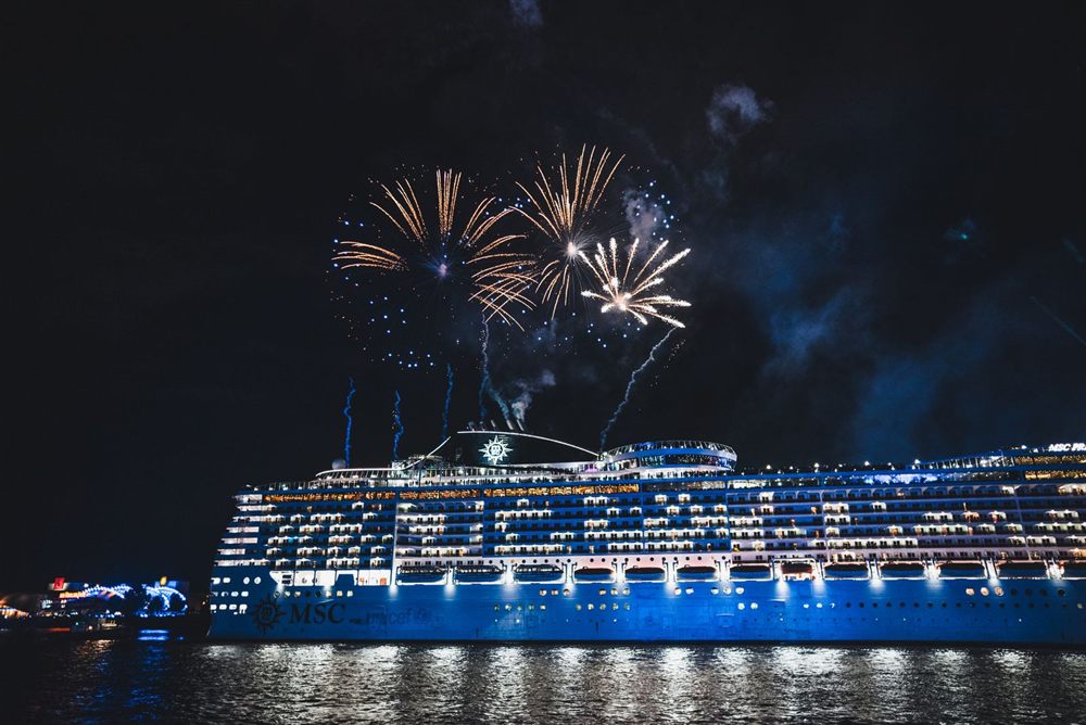 Brightly lit cruise ship under a burst of fireworks at night